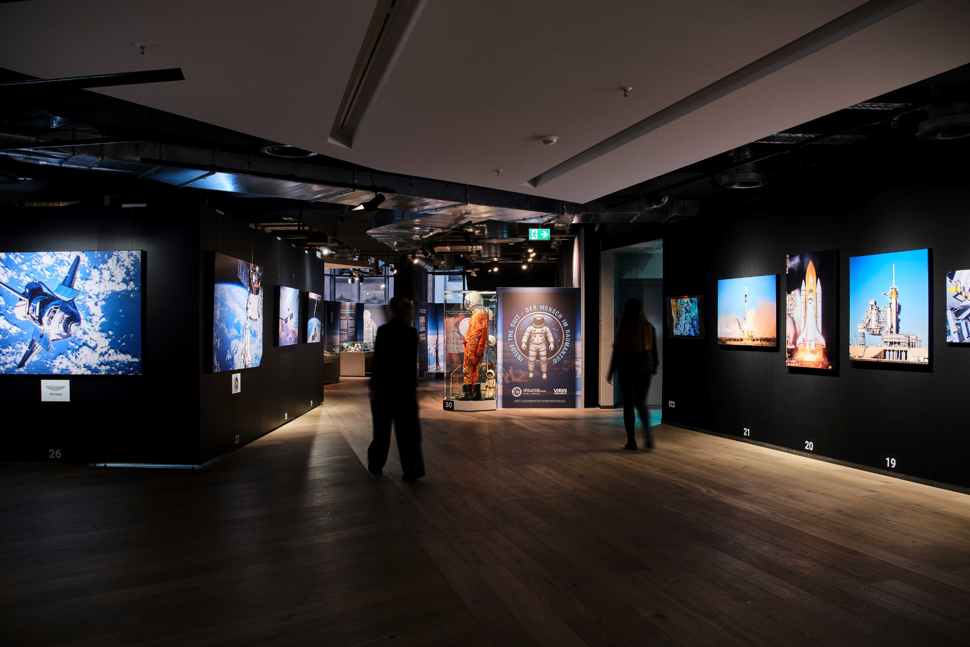 Visitors walking through the View From Above exhibition, with large backlit space photographs on dark gallery walls